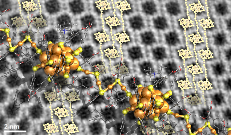 Electron microscopy image (background) of an ordered crystal consisting of 25-atom gold clusters. The data could be interpreted by a model of tightly packed polymeric chains of the clusters (light spheres). A close-up visualization of two such clusters, connected by a gold-ligand chain is shown in front. @ Sami Malola, University of Jyväskylä