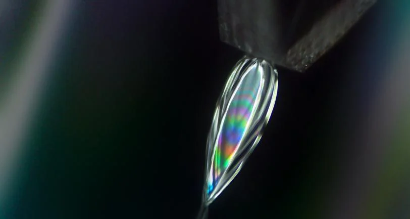 This microscope image shows color bands in a flat sheet of layered liquids shot from a tiny nozzle. The sheet is made up of outer layers of toluene, a solvent commonly used in paint thinners, and an inner water layer. @ David Hoffman/SLAC National Accelerator Laboratory
