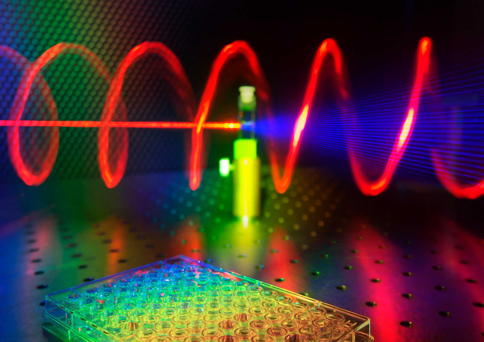 The illustration shows a microplate well in the foreground, while in the background a tested sample receives red laser light and releases twisted blue light. @ Ventsislav Valev, Kylian Valev and Lukas Ohnoutek, University of Bath