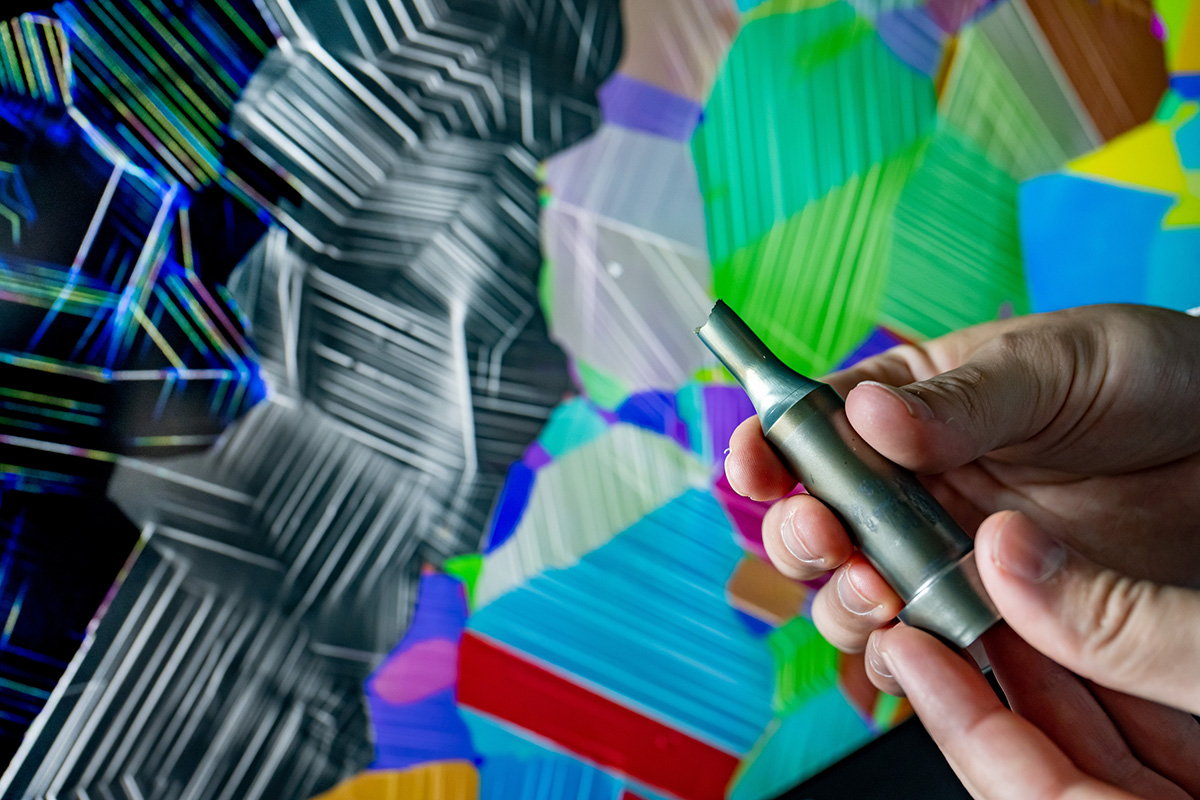 The foreground shows a fractured sample of an alloy used in aircraft engines. In the background, each color represents an orientation of the metal’s crystal structure. The gray lines indicate a specific measurement and inform how the metal deforms. The color of the lines indicates how intensely the atoms have been disrupted as a result of mechanical loading. @ Fred Zwicky