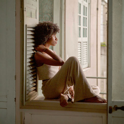 Woman sitting on a windowsill, gazing thoughtfully out, with soft natural light illuminating her.
