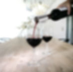 A man elegantly pouring red wine from a bottle into a glass at a dining table.