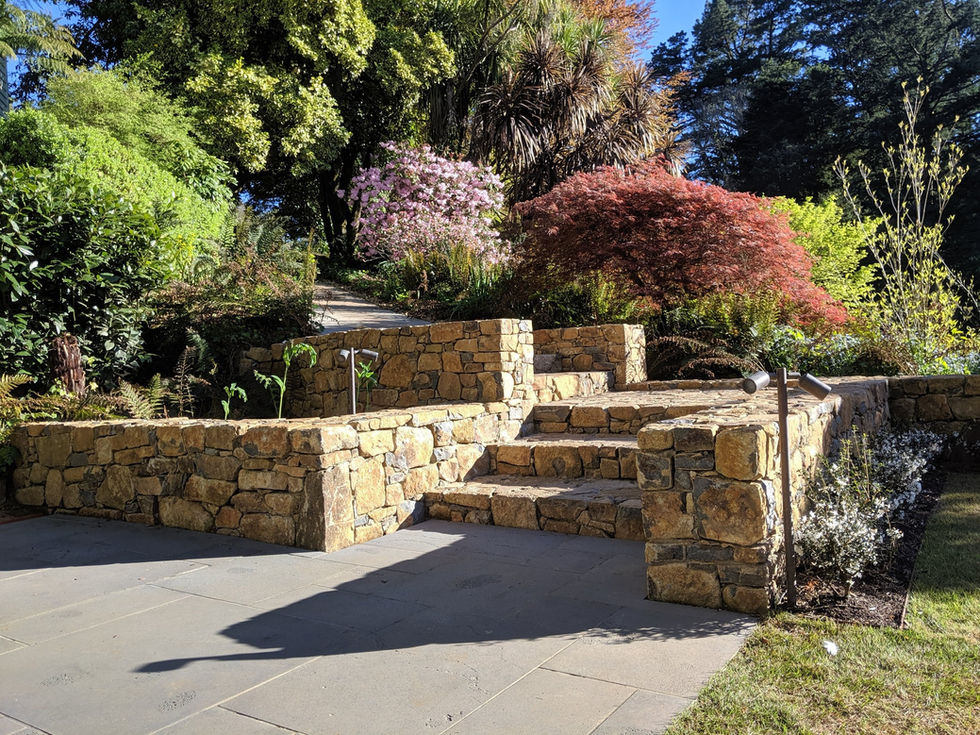 Stone steps and retaining wall connecting a lawn to a historic path, set within an existing mature garden and surrounded by layered planting.