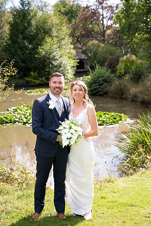 Bride and groom smiling and holding flowers in front of the boat house at The Ravenswood wedding venue..JPG