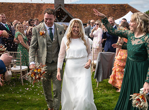 Bride and groom walking and covered in confetti. Lots of smiles and laughter. Montague Farm wedding venue..JPG