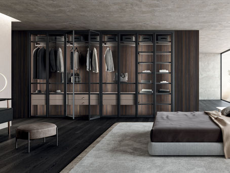 Moderan minimalistički spavaći prostor sa velikim garderoberom sa staklenim vratima, drvenim panelima, ugrađenim osvetljenjem i uredno organizovanom garderobom, koji odiše elegancijom.