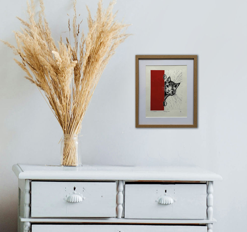 Framed artwork of peeping cat and dried flowers on white dresser.
