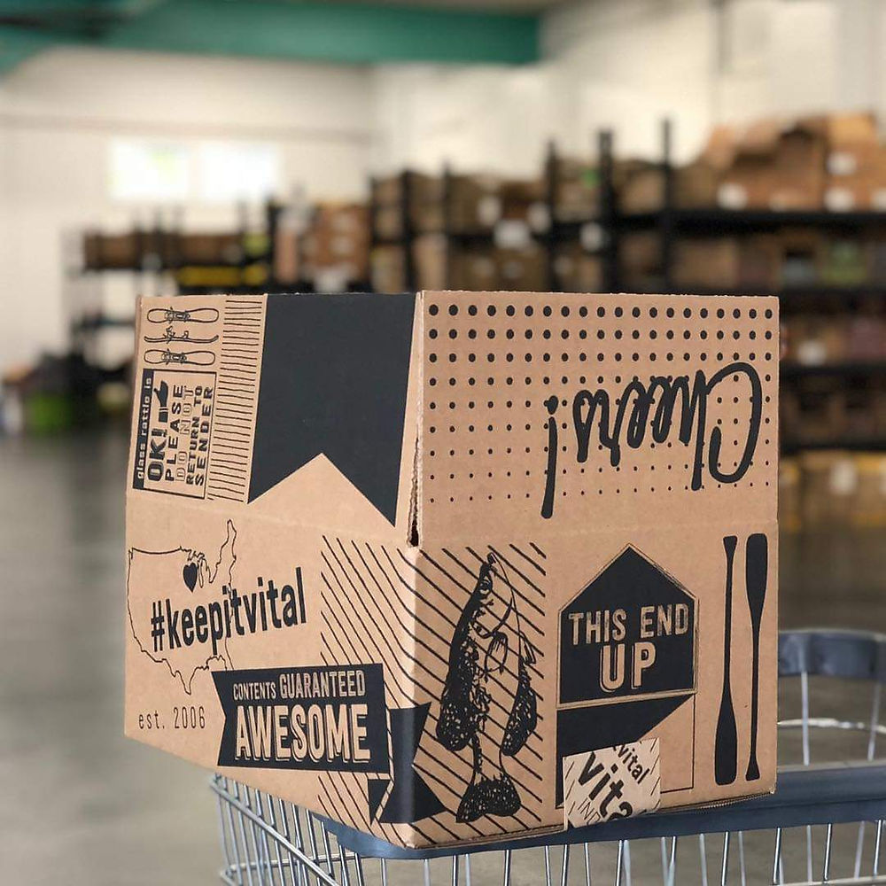 Decorated box with 'Cheers!' and '#keepitvital' in warehouse