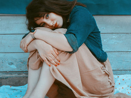A woman sits quietly on the dock, her arms wrapped around her knees, lost in contemplation.