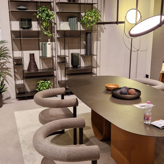 Elegantní jídelní kout s moderním stolem, zakřivenými čalouněnými židlemi a otevřenými policemi se zelení.