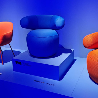 Výrazná expozice s barevnými čalouněnými křesly ve futuristickém modrém osvětlení na Salone del Mobile 2025.