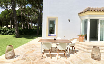 Dining table and chairs on sunny terrace next to the garden.