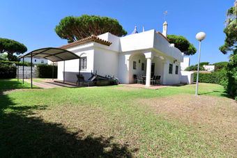 Modern Andalusian villa with green lawn and pine trees near the Atlantic Ocean.