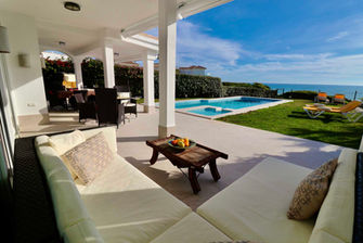 Cozy covered sitting area with pool and ocean backdrop.