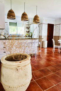 Kitchen with large island, hanging lamps and terracotta floor.
