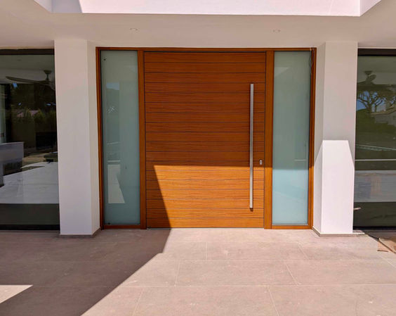 Solid wood front door surrounded by glass and white walls in modern Andalusian villa.