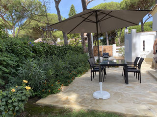 Patio with table, chairs and umbrella under pine trees.