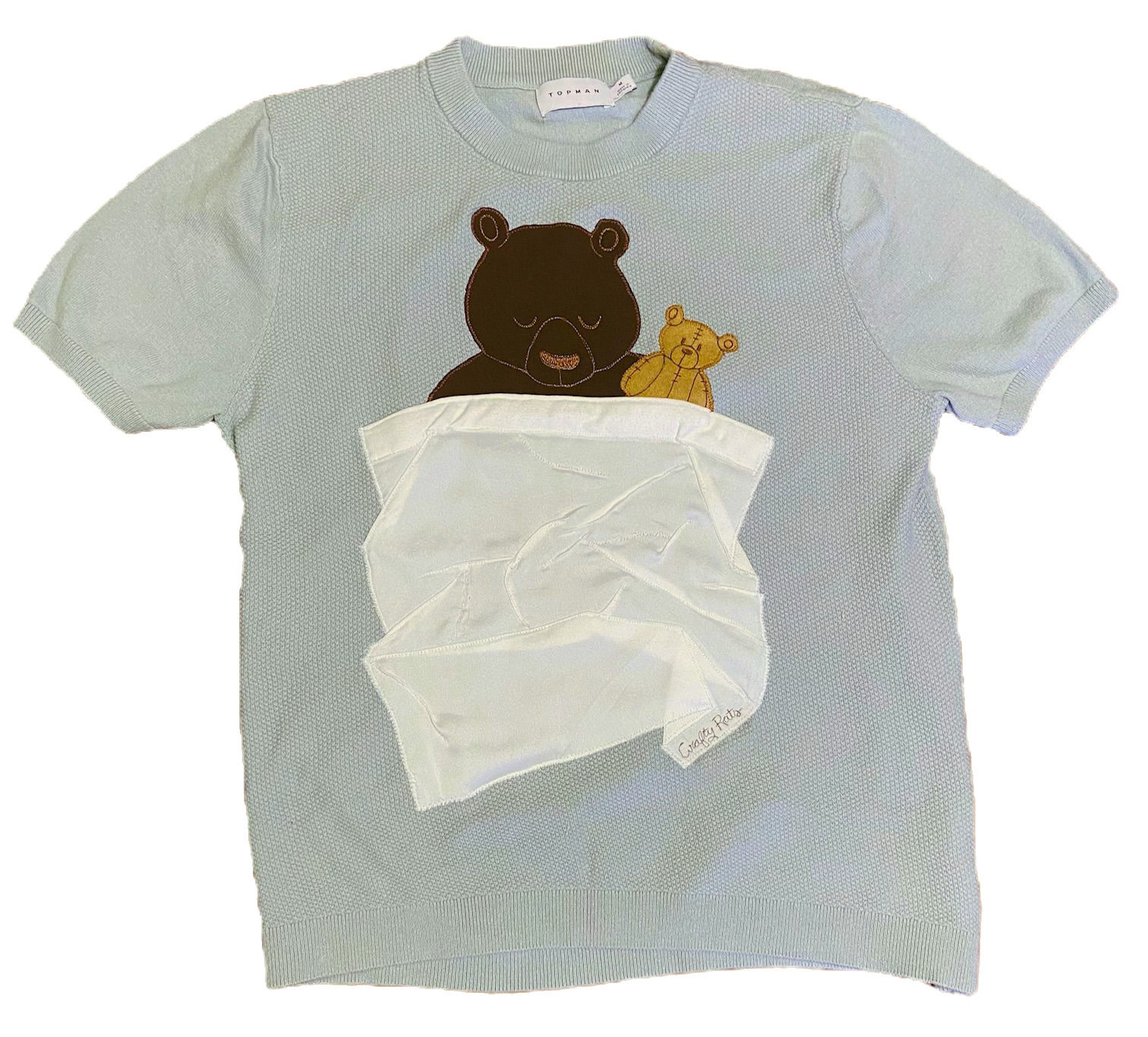 Pale seafoam green tee with applique bear and teddy bear tucked in a wrinkled blanket