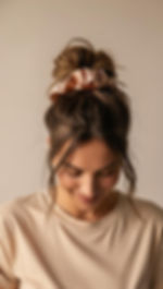 A woman wearing a beige Tshirt and scrunchy with messy bun