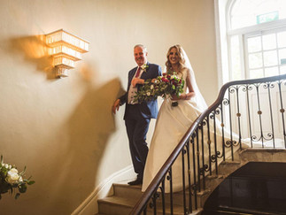 a bride and her father walk down the ornate stairs together at the maryborough hotel in cork