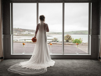 a bride is framed in a window with the sea outside