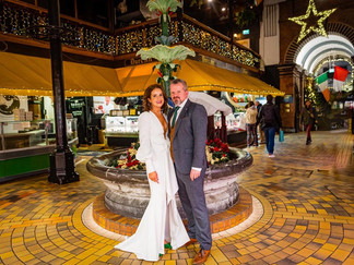 a bride and groom stand beside the fountain in the English Market in Cork City