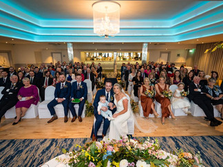 a bride and groom sit with their child and their guests after their wedding ceremony
