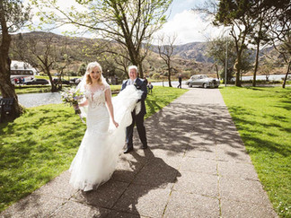a bride's father carries her dress as they walk to her wedding ceremony