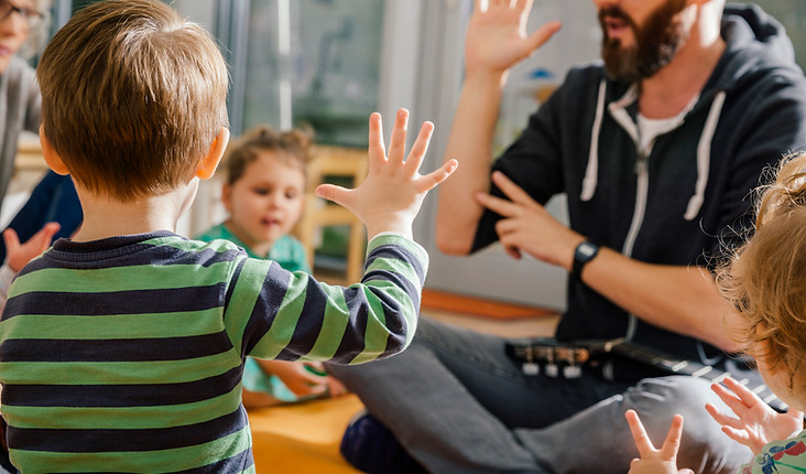 Enseignant accompagnateur faisant des gestes avec les mains, entouré d'enfants qui reproduisent le mouvement.