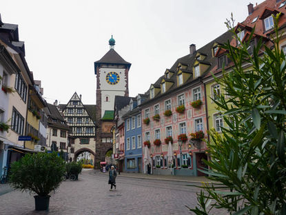 Rue pavée du centre historique de Fribourg-en-Brisgau, bordée de maisons colorées à colombages et de façades fleuries, avec la célèbre porte Schwabentor en arrière-plan.