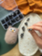 Main tenant deux yeux de sécurité ronds pour amigurumi, avec un hibou crocheté en arrière-plan.