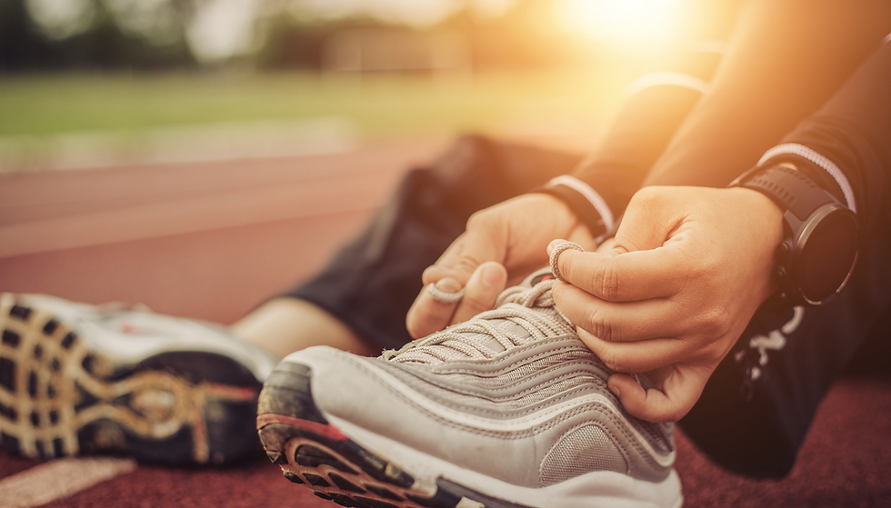 Close-up of a person tying silver sneakers on a sunlit track, wearing a black watch and dark clothing