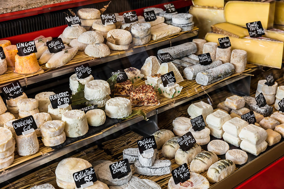 Cheese display in a shop, featuring assorted cheeses with labels showing names and prices. Warm lighting creates an inviting atmosphere.
