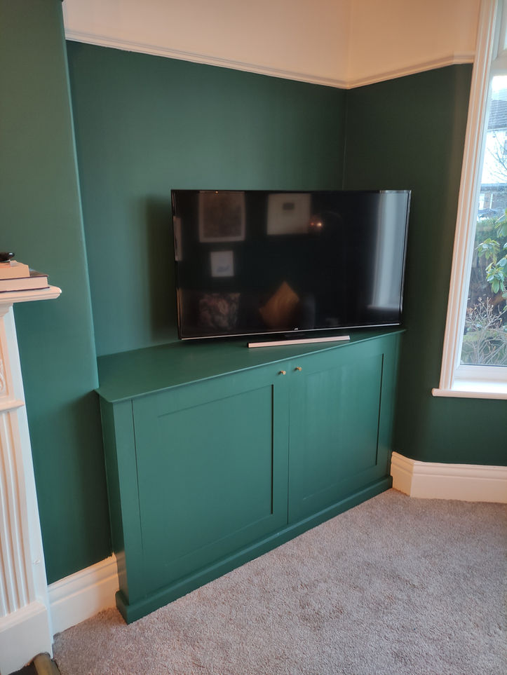 Custom built-in dark green alcove cupboards with concealed storage, fitted into a corner living room space.