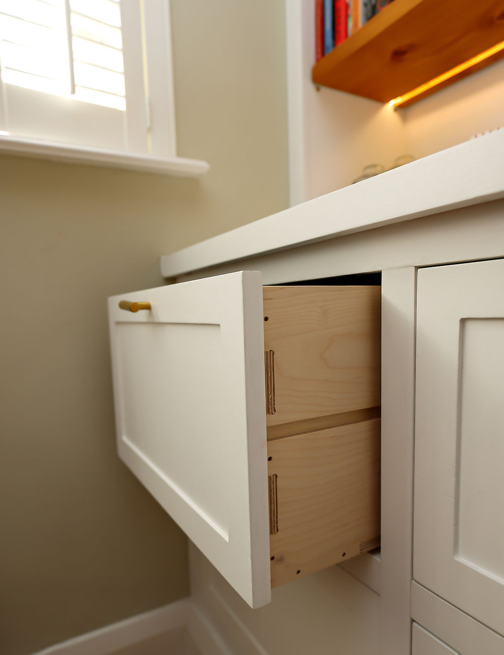 Close-up of two wooden drawers in a painted shaker-style kitchen cabinet, showcasing joints and brass handles, highlighting craftsmanship and quality materials.