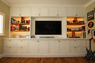 Bespoke media wall by Koa Design featuring painted shaker cabinetry, integrated oak shelving with LED lighting, and built-in storage for a modern living room entertainment setup.