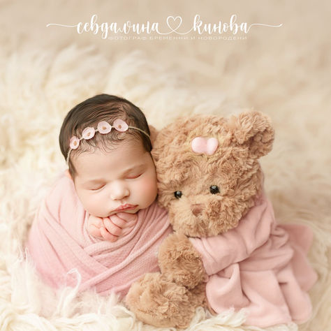 Newborn baby wrapped in a soft pink photography wrap, wearing a floral headband and resting beside a teddy bear.