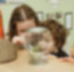 Woman and child closely observe plant leaves in a clear jar.