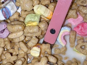 Close-up photo of Lucky Charms cereal, featuring toasted oat cereal pieces and colorful marshmallow shapes sitting in milk with a pink spoon inside the bowl.