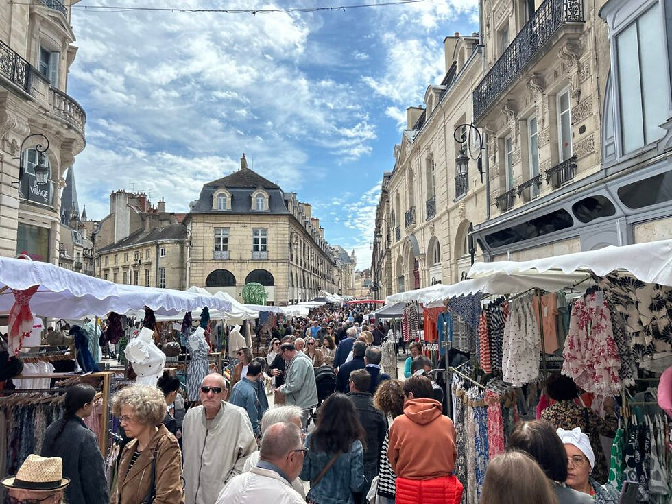 Marché en plein air dans le centre historique de Dijon, avec des étals de vêtements et une foule animée dans une rue bordée d’immeubles en pierre.
