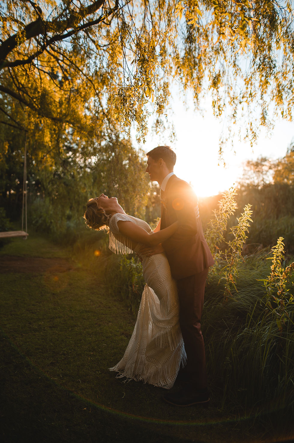 Lolly & Jonny hold each other laughing by a lake with a stunning sunset at Lake Henry, Richmond.