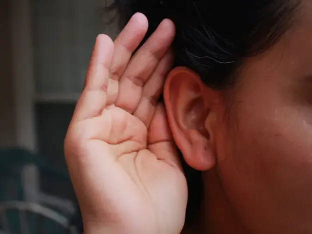 Mujer con la mano en la oreja representando la acción de escuchar atentamente