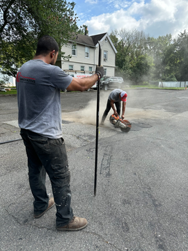 Crew member from Innovative Home Improvement using a saw machine on the road for a construction project.