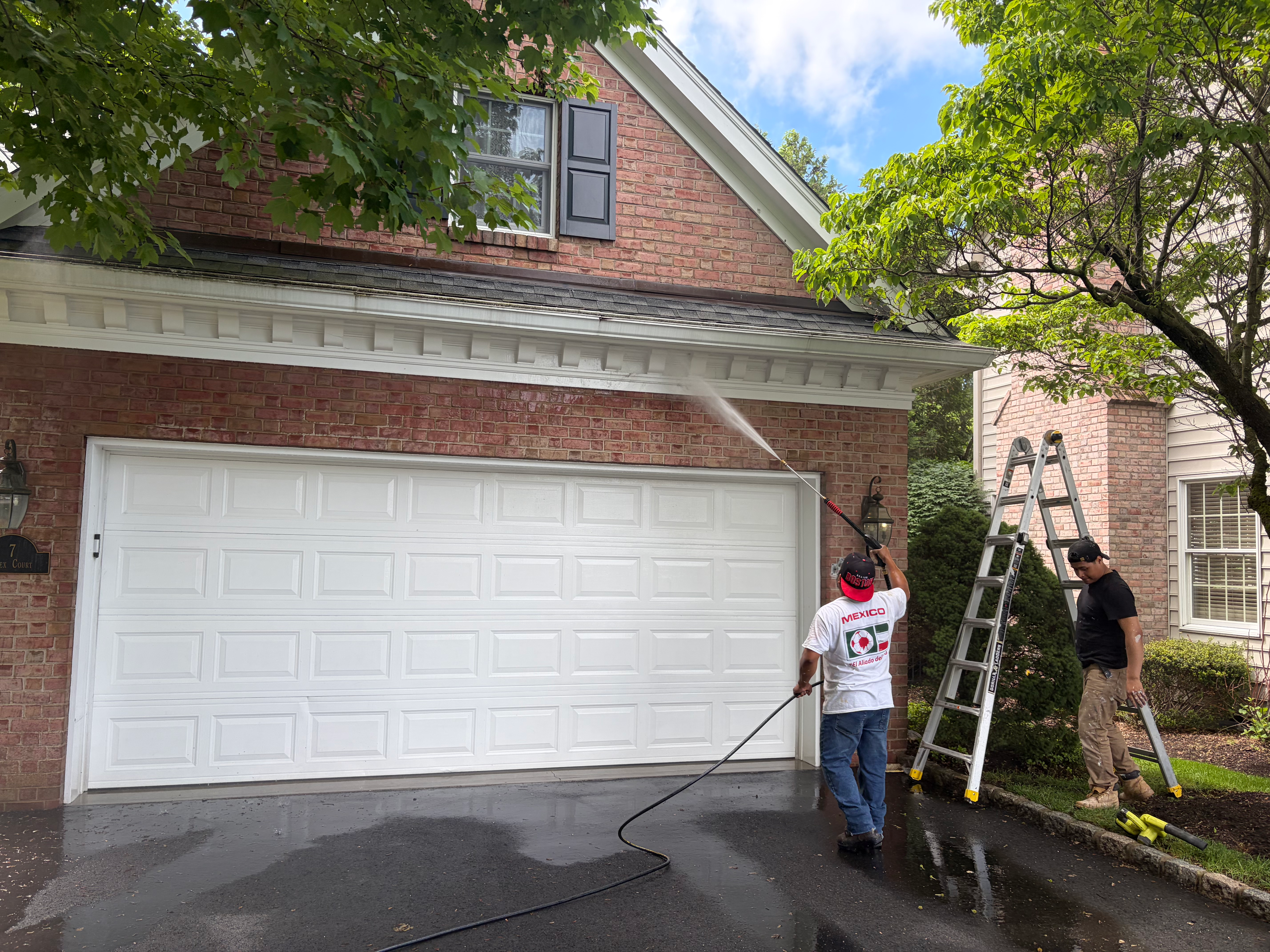 Crew power washing exterior in Bergen County, NJ — soft-wash on brick siding plus ladder access for upper trim cleanup
