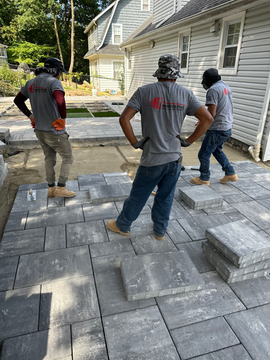 Three crew members from Innovative Home Improvement working on a backyard patio installation.