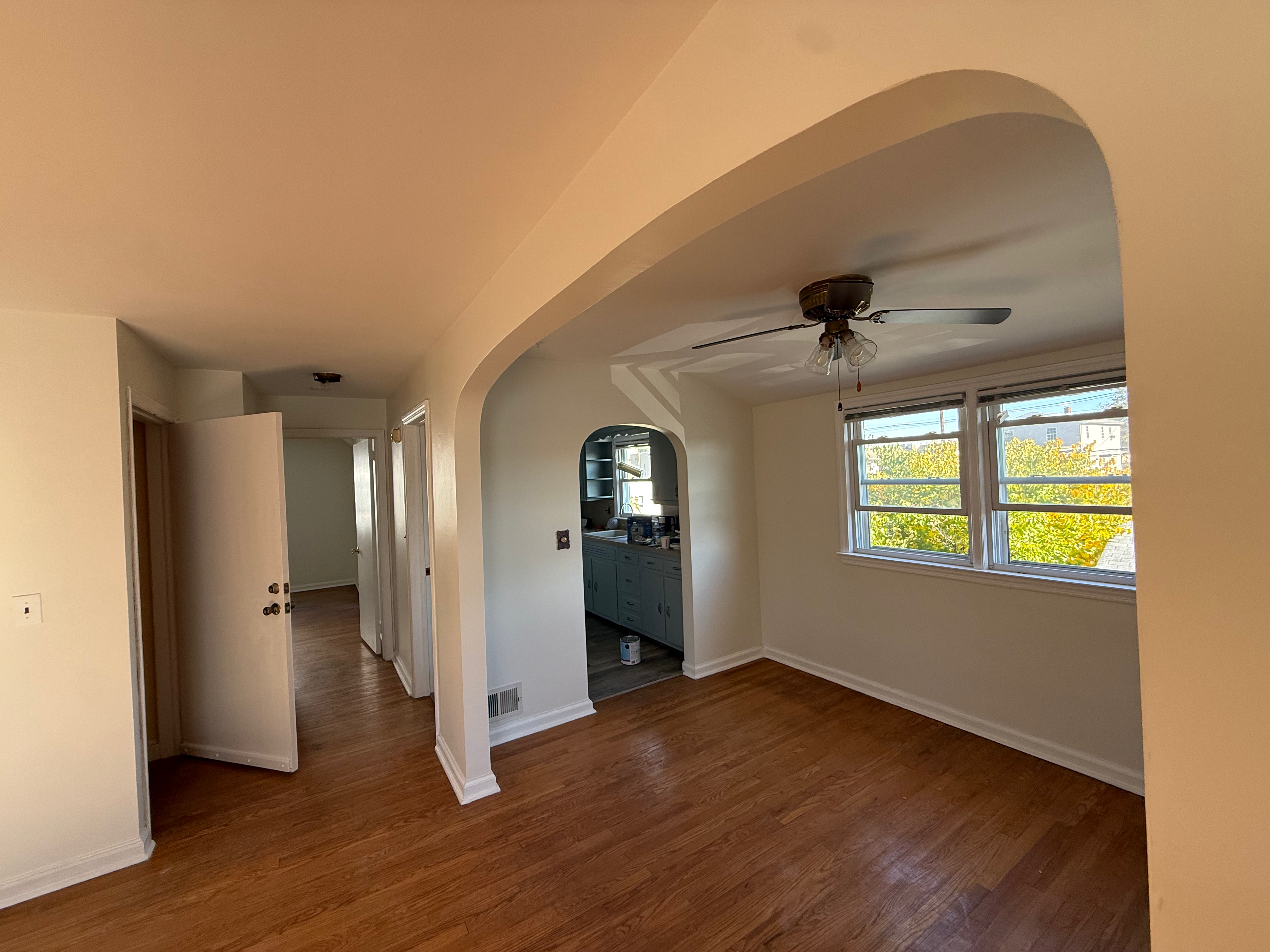 Open dining-to-kitchen view after full interior repaint in Bergen County, NJ — clean cream walls, dark hardwood, original arched doorways
