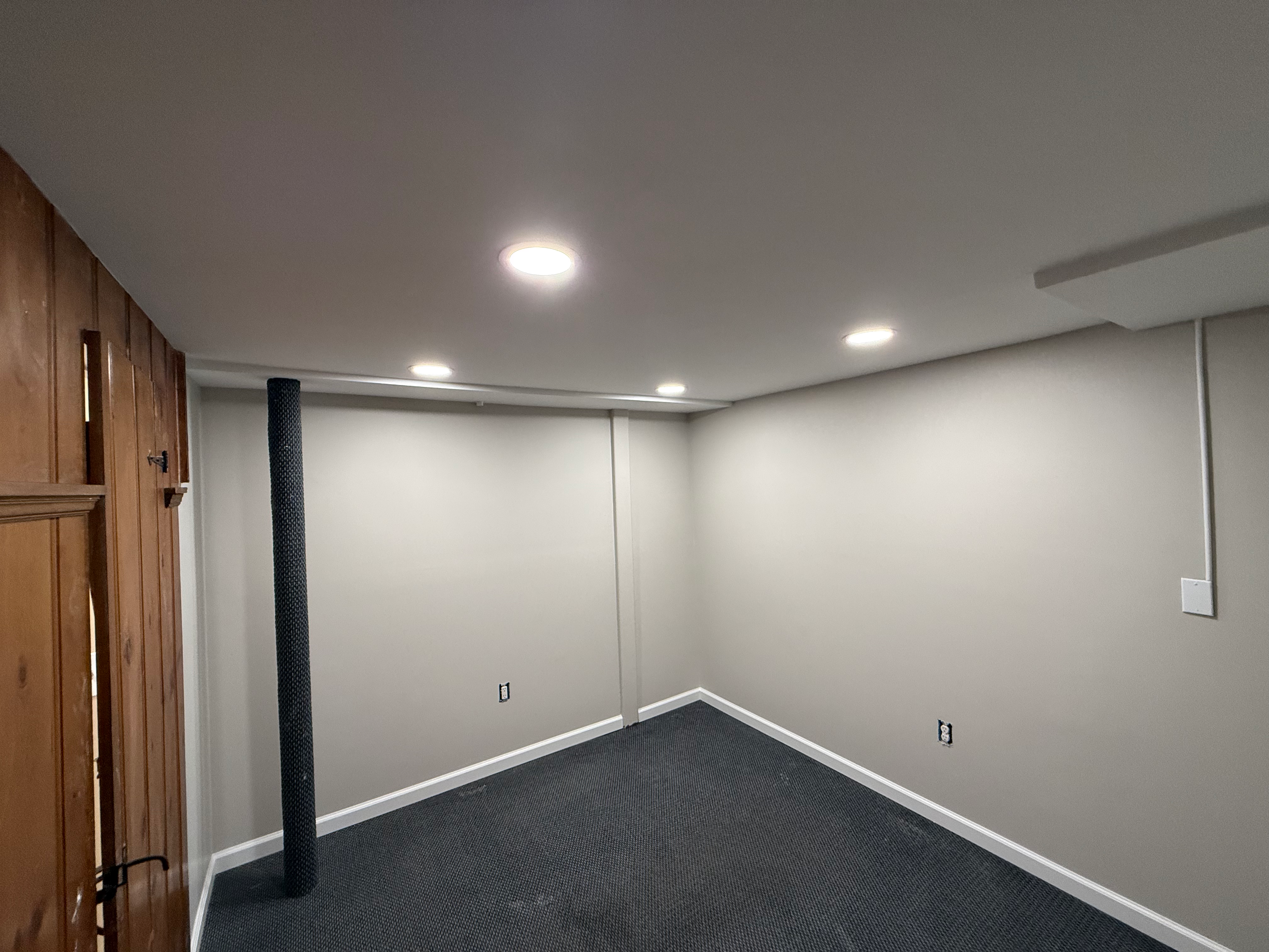 Finished basement rec room in Bergen County, NJ — recessed lighting, painted support pole, and modern carpet finish