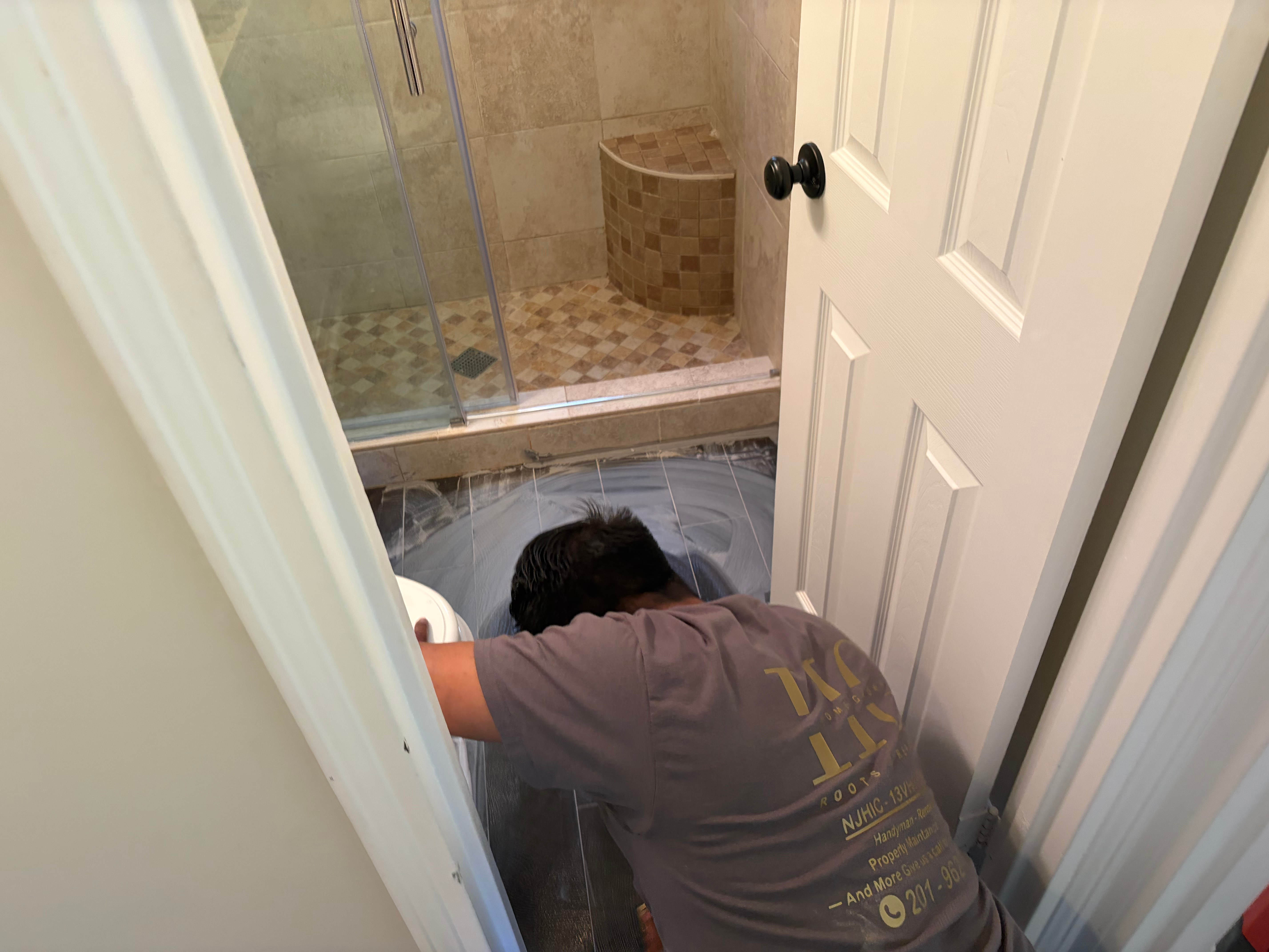 Tile floor install in Bergen County, NJ — HomeGrown contractor setting tile against an existing beige stone shower