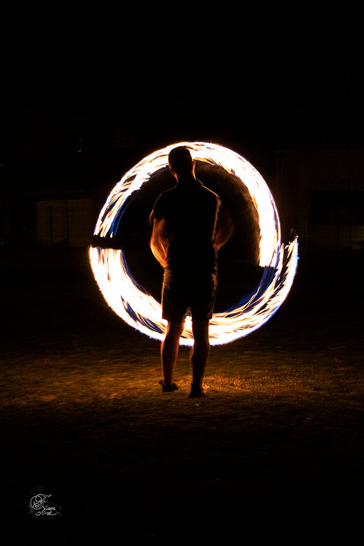 Silhouette de personne maniant le feu avec un cercle lumineux dans la nuit.