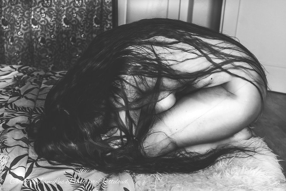 Femme avec longs cheveux noirs et corps recroquevillé sur le lit. Reflets De Fawn.